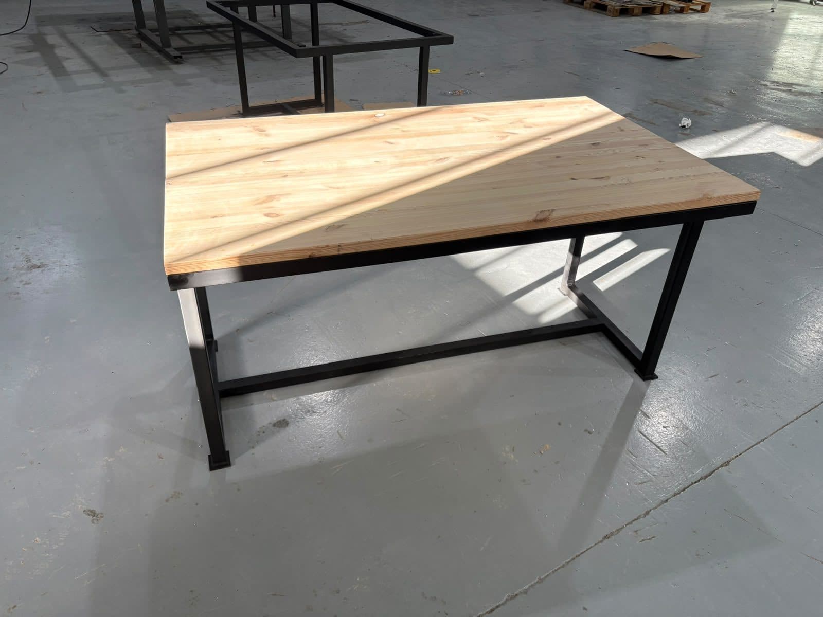 Mesa con estructura de acero negra y tablero de madera en una nave
