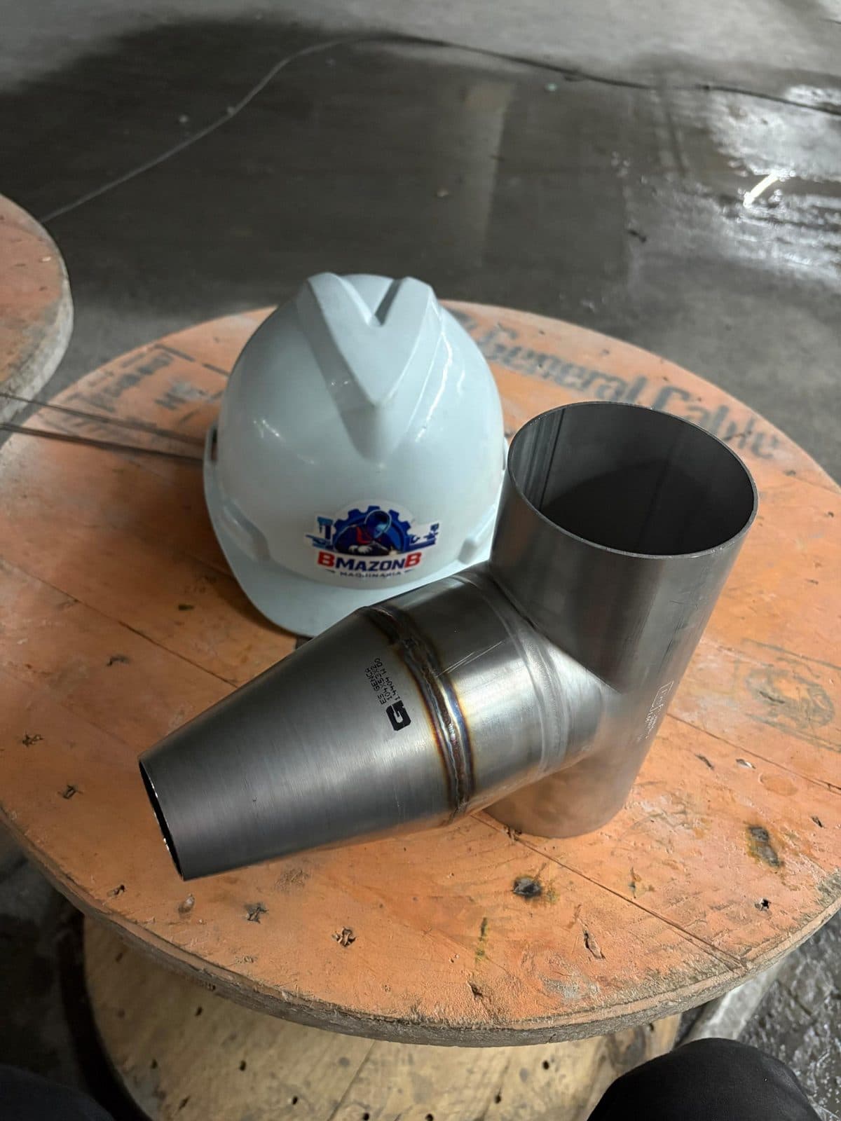 Derivación en Y de tubo de acero inoxidable junto a un casco con el logo de BMAZONB